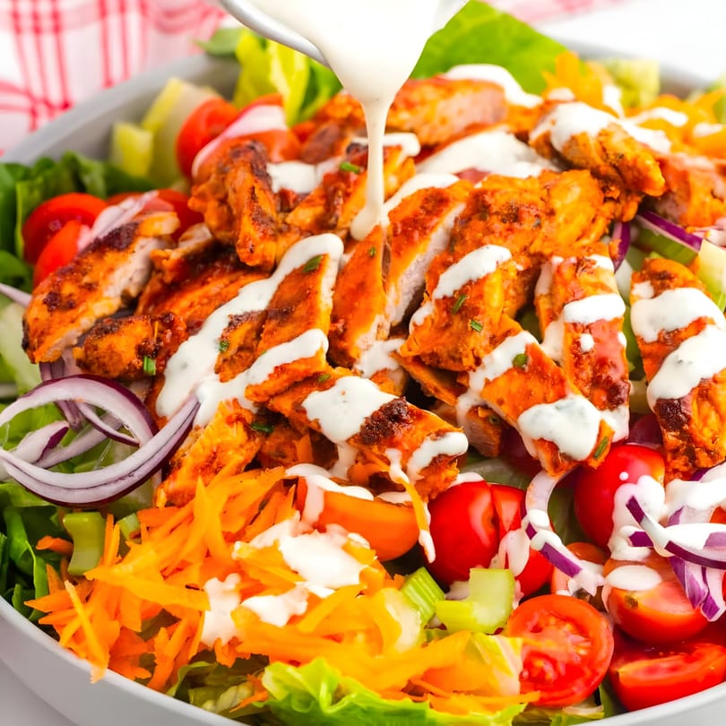 Ranch dressing drizzled over a vibrant salad with grilled chicken, lettuce, tomatoes, red onions, and carrots.